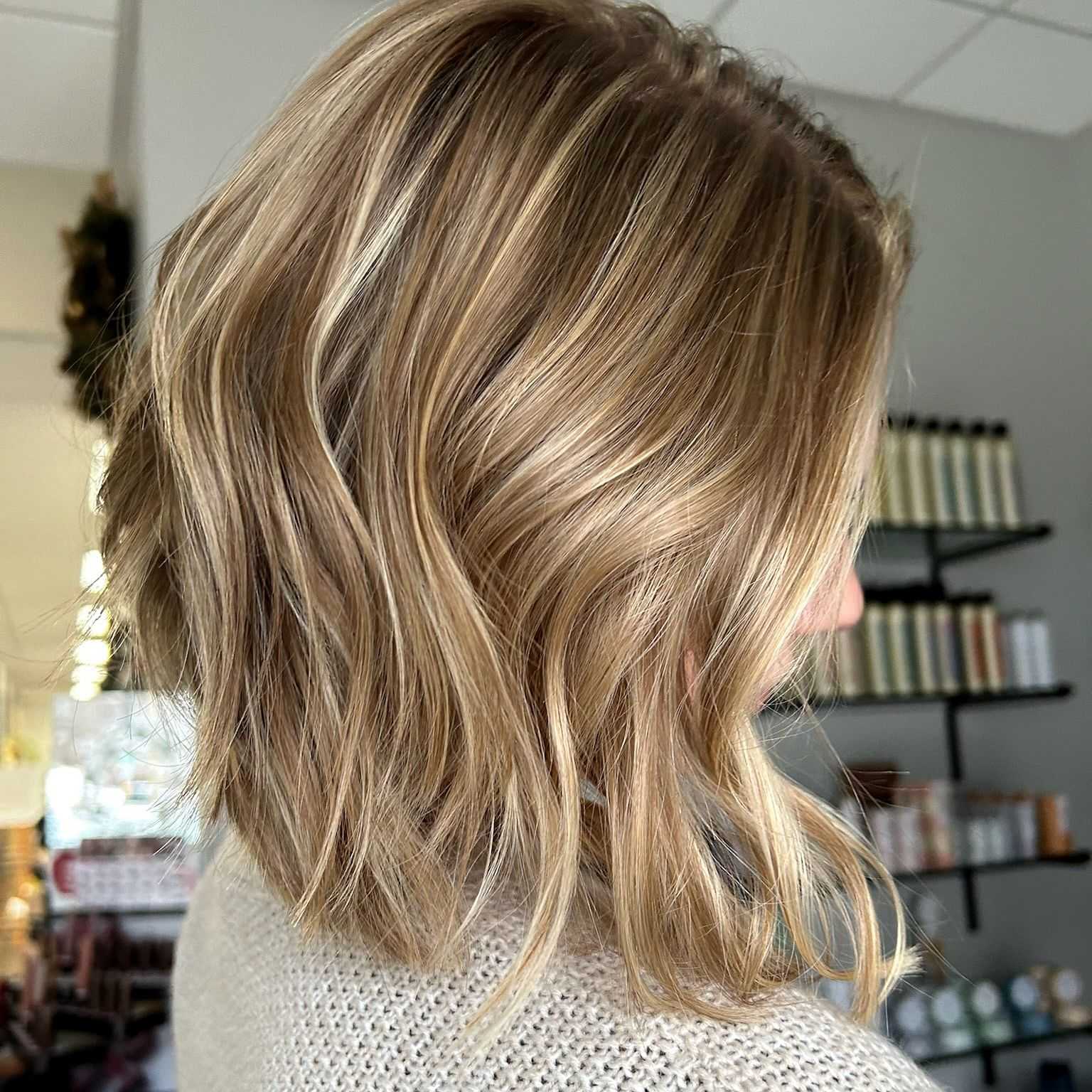 Close-up of a woman with shoulder-length blonde hair styled in soft waves, inside a salon.